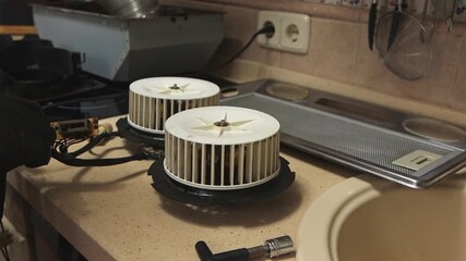 Close-up of two extractor fan blower motors being tested on a kitchen countertop during repair.