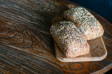 Two multigrain artisan bread loaves resting on a wooden cutting board over a rustic table. Warm natural lighting highlights texture. Ideal for bakery, organic food, healthy eating, and culinary themes