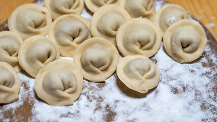 Dumplings on a wooden board with flour in the background. Close-up of homemade dumplings. Natural products and family traditions of dumpling cooking. High quality photo