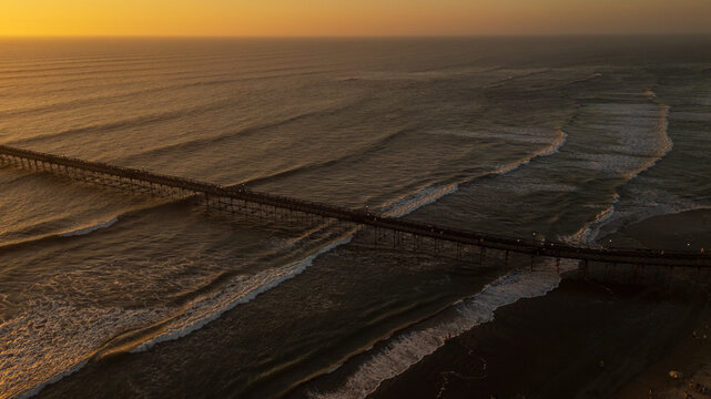 Sunset beach scene in Pimentel, Peru, with warm golden light, gentle waves and swimmers enjoying the ocean near the iconic pier. Perfect for travel and summer tourism content - Powered by Adobe