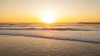 Obraz premium Sunset beach scene in Pimentel, Peru, with warm golden light, gentle waves and swimmers enjoying the ocean near the iconic pier. Perfect for travel and summer tourism content
