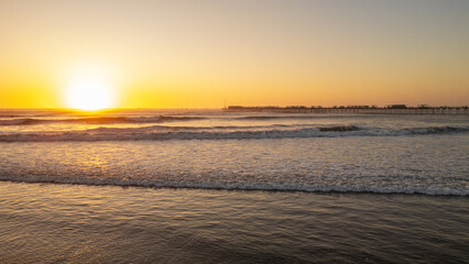 Sunset beach scene in Pimentel, Peru, with warm golden light, gentle waves and swimmers enjoying the ocean near the iconic pier. Perfect for travel and summer tourism content