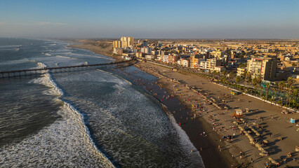 Drone photos of Pimentel Beach, Peru, capturing the pier, rolling waves and crowds enjoying a warm summer day on the northern coast. Ideal for travel, tourism and coastal destination content
