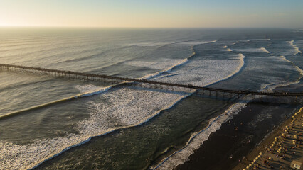 Sunset beach scene in Pimentel, Peru, with warm golden light, gentle waves and swimmers enjoying the ocean near the iconic pier. Perfect for travel and summer tourism content