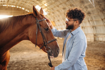 Side view, stroking the animal. Man is with horse in the hangar