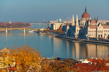 Fototapeta premium Budapest cityscape, panoramic view of city and Danube River, Parliament building with Margit bridge and beautiful architecture in autumn season, trees, branches and yellow leaves in foreground