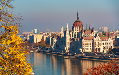Fototapeta premium Budapest cityscape, panoramic view of city and Danube River, Parliament building and beautiful architecture in autumn season, trees, branches and yellow leaves in foreground