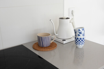 Electric kettle and ceramic mugs on minimalist kitchen counter. Contemporary home aesthetics, Scandinavian style, and cozy morning coffee or tea preparation concept