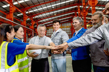 Group of happy engineers join hands together while standing in manufacturing factory. Corporate...