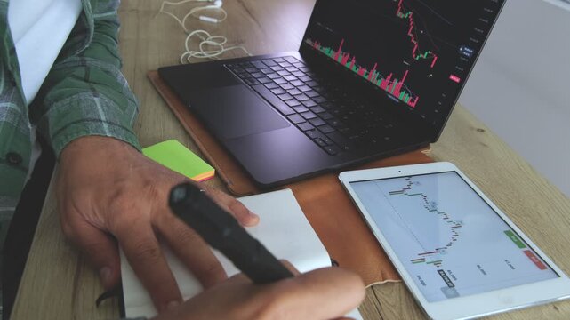 Male hands writing investment notes about etf, crypto, and stock market on a notebook at his desk