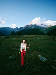 Fototapeta premium Mountain landscape, outdoor scene with a woman wearing red pants standing in a meadow, distant peaks, clear sky, rugged terrain and calm atmosphere, ideal for travel, exploration and nature