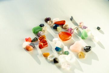 Assorted polished gemstones in vibrant colors lie on a bright surface, casting soft shadows and...