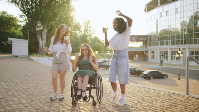 three female multiracial friends one inclusive woman in a wheelchair enjoying drinks and dancing together outdoors at sunset in a vibrant urban setting - Powered by Adobe