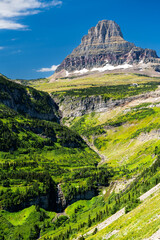 Reynolds Creek flows through green valley below Clements Mountain in Glacier National Park, Montana. Scenic landscape features waterfall and rocky peaks in UNESCO World Heritage site