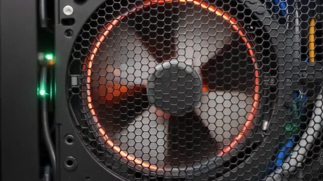 Close-up of a computer case fan with red LED lights illuminating its blades and protective grill