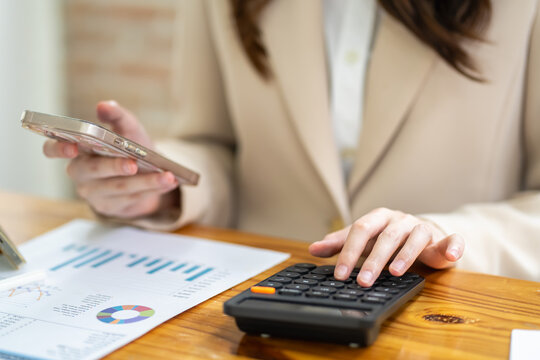Businesswoman using smartphone and calculator for financial analysis in office professional environment close-up view