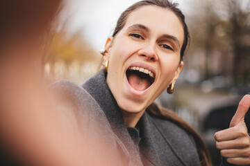 Close up widely smiling woman tourist show thumb up like gesture, walking near canal. Happy young...