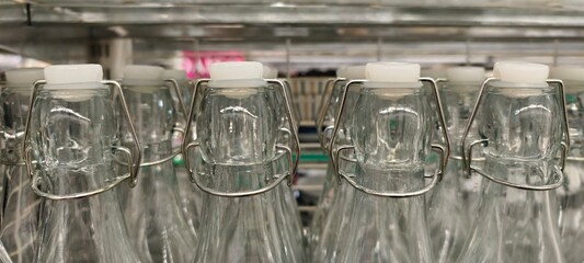 Clear glass bottles with white swing-top caps and metal wire clasps, neatly arranged on a shelf.Close-up retail display highlights the uniformity, transparency, and functional elegance of reusable.