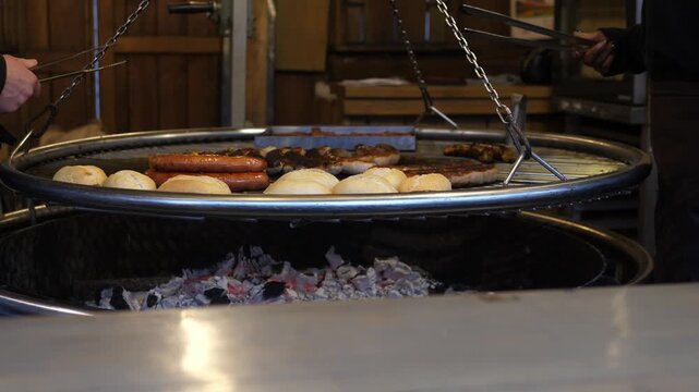 Large round grill with sausages, bread rolls and meat cooking over hot coals. Traditional outdoor barbecue at a winter or street market.