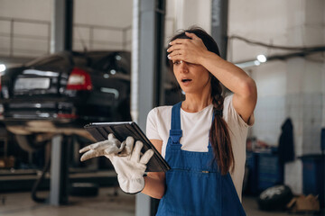 In shock, something went wrong, with digital tablet. Female mechanic is working in the modern car workshop