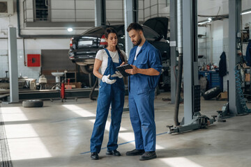 Data is in the digital tablet. Auto repair shop employees are working together. Man and woman