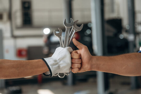 Side close up view of male and female's hands with tools in car repair station - Powered by Adobe