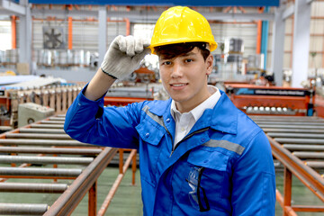 Portrait of young male worker with safety clothing and helmet touching hard hat at manufacturing factory. Engineering staff working in industry manufacturing site. Industrial worker works in factory