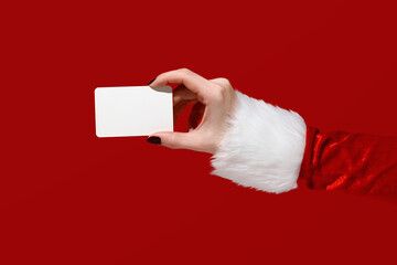 Womans hand in Santa sleeve holding blank card on red background. Christmas mockup.