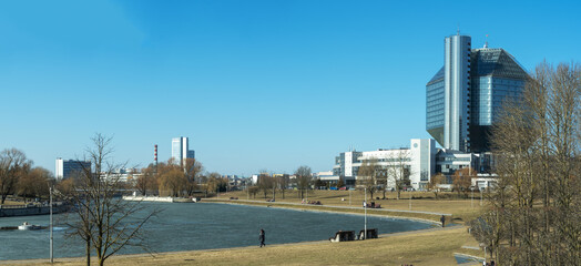 Dialogue between nature and geometry expressed in quiet riverside scene with modern architecture and bare trees. National library of Belarus in Minsk with modern glass architecture.