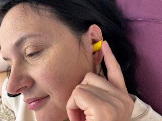 Close up of adult brunette woman inserting yellow earplugs, noise protection for healthy sleep, deep rest, insomnia prevention and peaceful home bedroom atmosphere