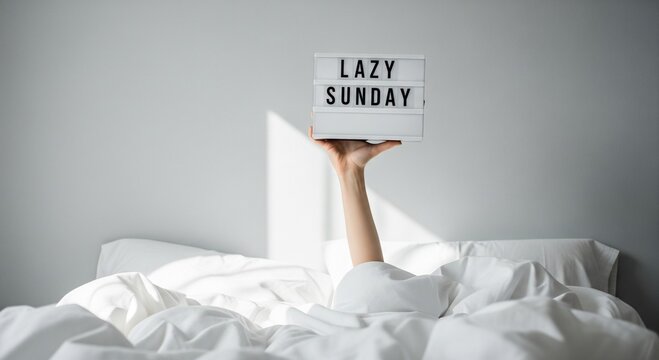 Hand holding lightbox sign that says lazy sunday in bed