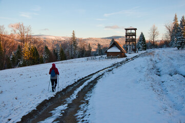 Górski zimowy szlak z wędrowcem, turystyczną chatą i wieżą widokową z widokiem na mroźny las o zachodzie słońca. Zimowy szlak na Stary Groń w Beskidzie Śląskim. © Pol Badger