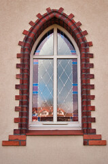 Eleganckie, łukowate okno z kolorowymi witrażami osadzonymi w ceglanej ramie na beżowej ścianie zewnętrznej.