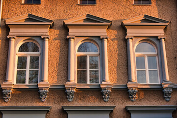 Trzy łukowe okna z ozdobnymi kolumnami na oświetlonej słońcem fasadzie budynku o złotej godzinie. © Pol Badger