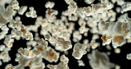 Dynamic macro shot of flying popcorn pieces against a black background. Crisp detail and motion captured in a dramatic, high-contrast composition. Perfect for advertising or creative design.