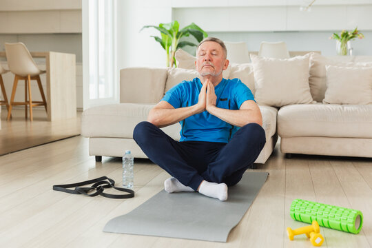 Yoga mindfulness meditation. Senior adult mature man practicing yoga at home. Mid age old grandfather sitting in lotus pose on yoga mat meditating relaxing. Older man doing breathing practice - Powered by Adobe
