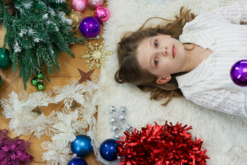 Girl holding ornament up on rug with holiday items