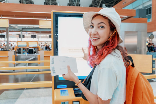 Tourist engaging with a self service check-in machine at the airport, printing her tickets and boarding pass - Powered by Adobe