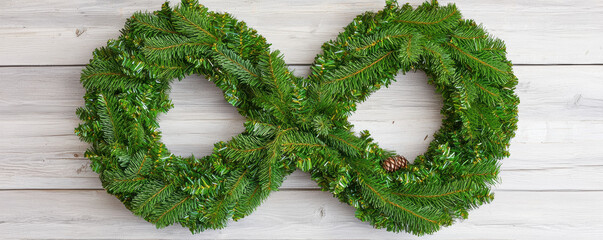 Christmas wreath made of green pine branches shaped like infinity symbol on white wooden background festive decoration