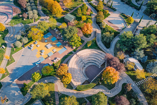 Urban park featuring an open air amphitheater, winding pathways, colorful trees, and recreational areas from an aerial perspective during autumn