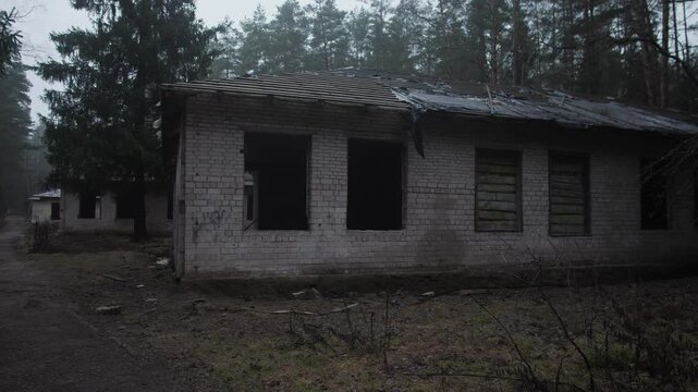 Row Of Abandoned Brick Buildings Beside Muddy Path, Boarded Windows And Dark Openings, Misty Tree Line Behind, Mood Heavy With Isolation And Slow Nature Reclaiming Structure