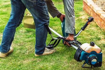 Brush cutter or shoulder strap mower and green gallon of gasoline on lawn with green grass before cutting. Petrol brush cutter, grass cutting. Backpack mower or lawn mower for mowing grass and shrubs.