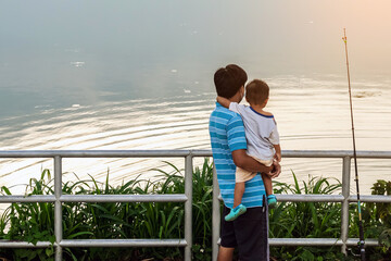 Father with son stand on pier and catching fish on lake background. Family fishing together on pond. Family fishing holiday. Dad with child outdoors near river. Father and boy son fishing together