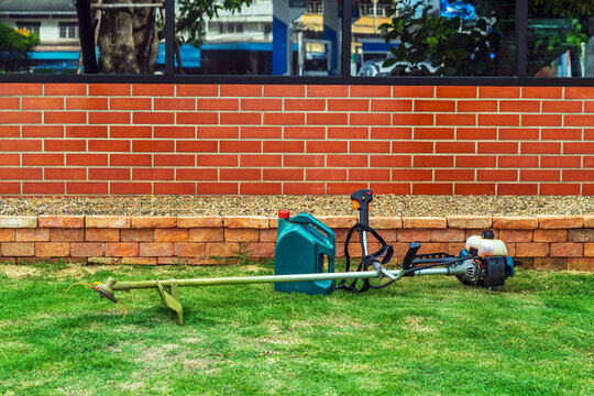 Brush cutter or shoulder strap mower and green gallon of gasoline on lawn with green grass before cutting. Petrol brush cutter, grass cutting. Backpack mower or lawn mower for mowing grass and shrubs.