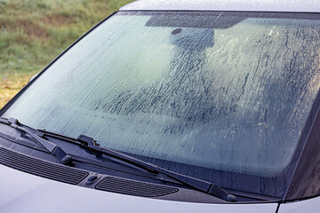 Obraz premium Car windshield covered in thick ice and frost on a cold winter morning, needing scraping before driving