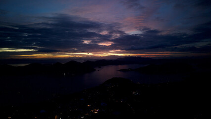 Fototapeta premium High altitude night aerial panoramic view of Coron Bay islands and coastal town lights in Palawan, Philippines, during blue hour twilight under dramatic cloudy sky over calm sea.