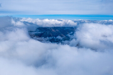 A breathtaking winter mountain landscape covered in deep snow, with dramatic clouds rolling over rugged alpine peaks under a bright blue sky, creating a serene and powerful natural atmosphere.