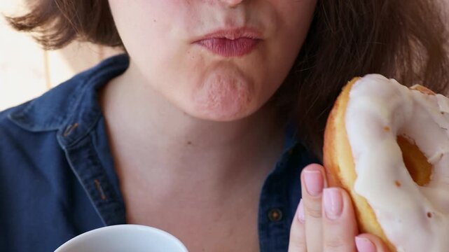 Caucasian woman eating donut with tea in a mug close up