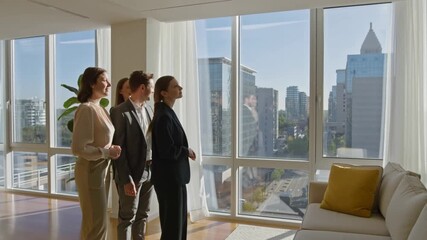 Four professionals looking out a large window, enjoying a city view. The group, likely a team, stands in a modern, well-lit space. Stock Video - Powered by Adobe