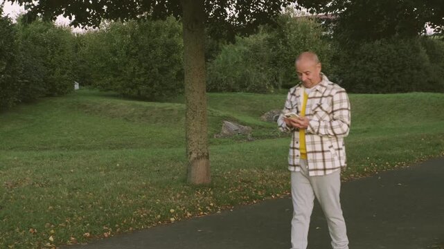 Positive elderly white man 65 years old enjoying technology, senior using modern smartphone, joyful moment surrounded by peaceful nature